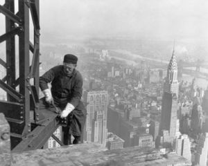 A man working on a steel girder high about a city skyline.